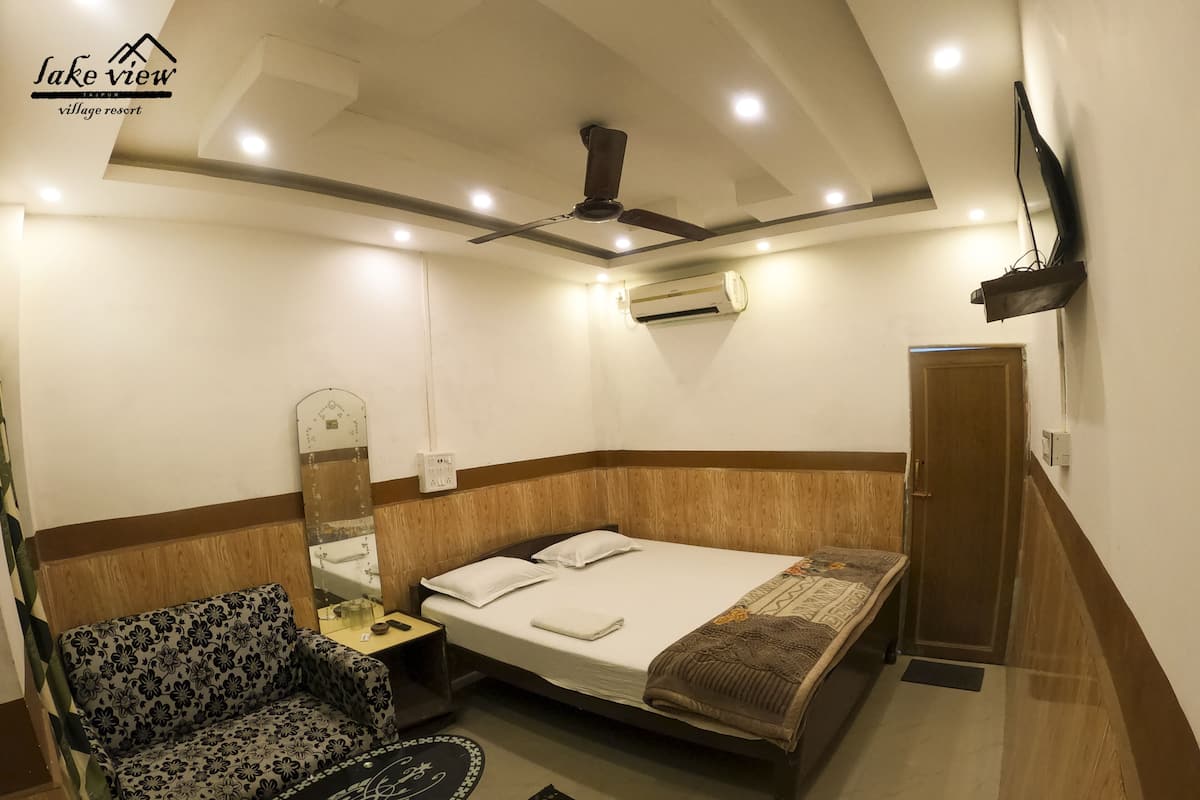 A hotel room with a bed, a sofa, a small table, a mirror, a TV mounted on the wall, and a ceiling fan.