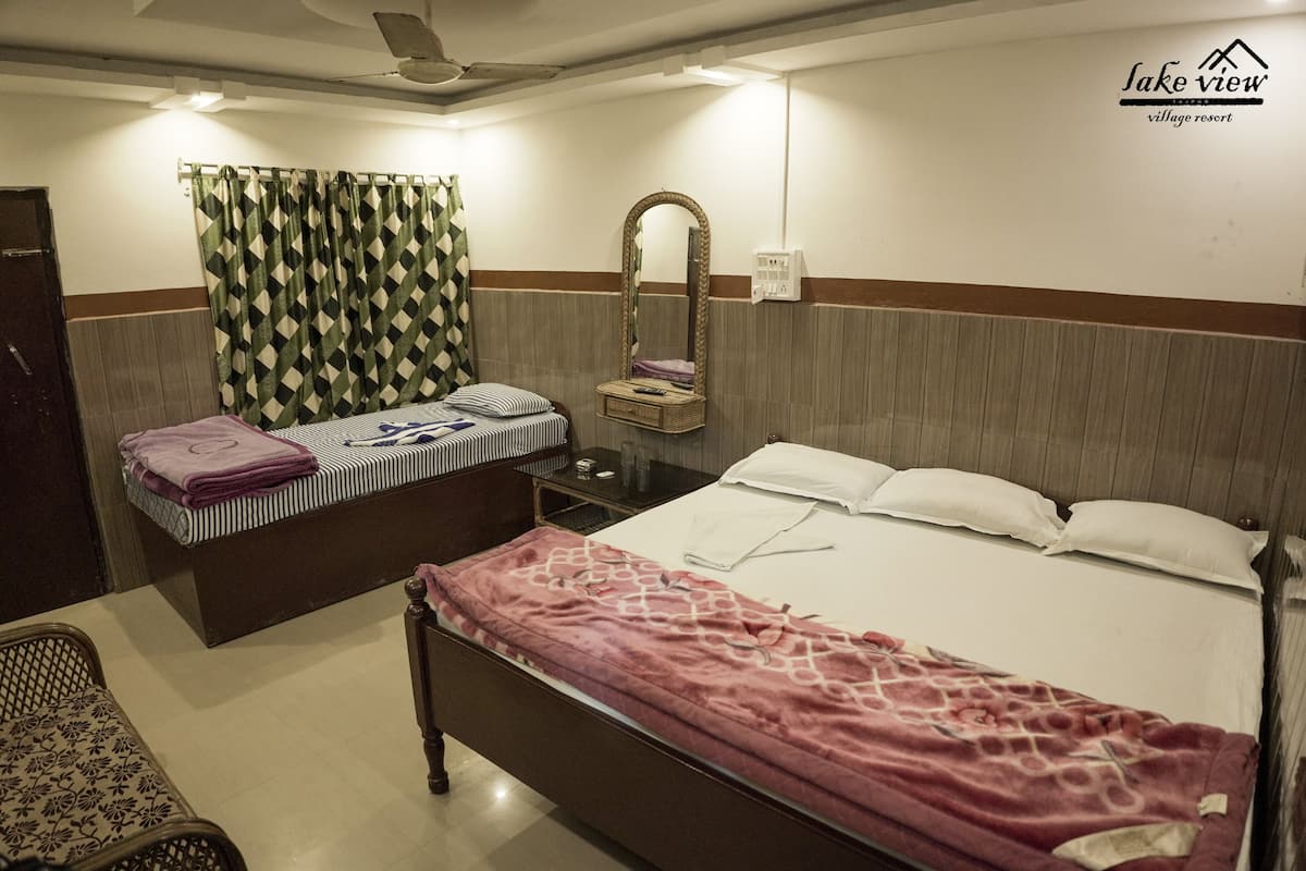 A hotel room with a bed, a bedside table, a mirror, a window with curtains, and a ceiling fan.