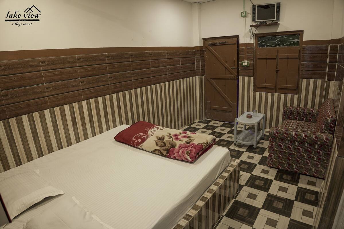 A hotel room with a bed, a small table, a chair, and a TV mounted on the wall.