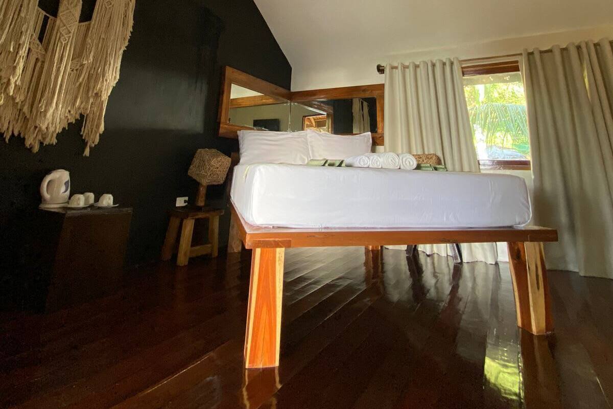 Quarto com cama de madeira, ventilador de teto, espelho grande e janela com cortinas.