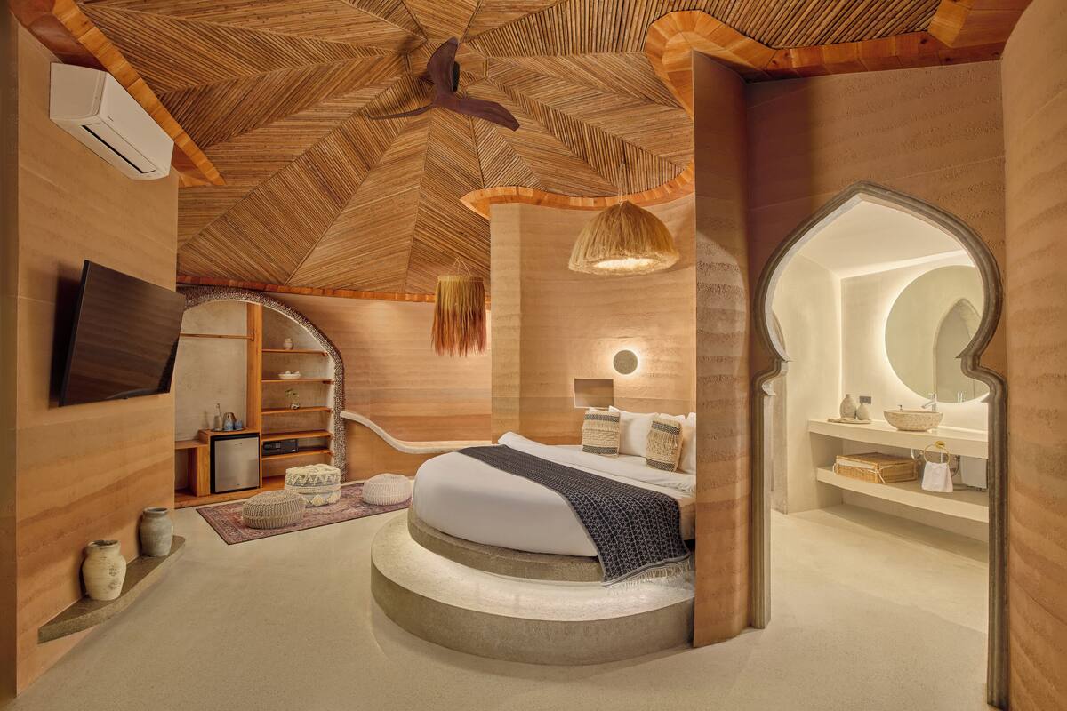 Quarto moderno com teto de madeira, cama redonda, guarda-roupa embutido e banheiro com espelho grande.