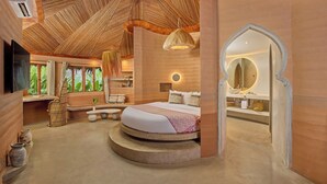 Une chambre à coucher avec un lit placé au centre d’une plateforme circulaire, un grand miroir et une vue sur la verdure par les fenêtres.