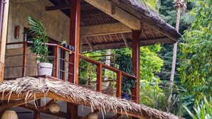 Un bâtiment rustique en bois, doté d’un toit de chaume, entouré d’une végétation luxuriante et de palmiers.