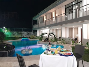 A poolside dining area with a table set for a meal, surrounded by a pool and a building with a balcony. - Francisco Resort (Panglao)