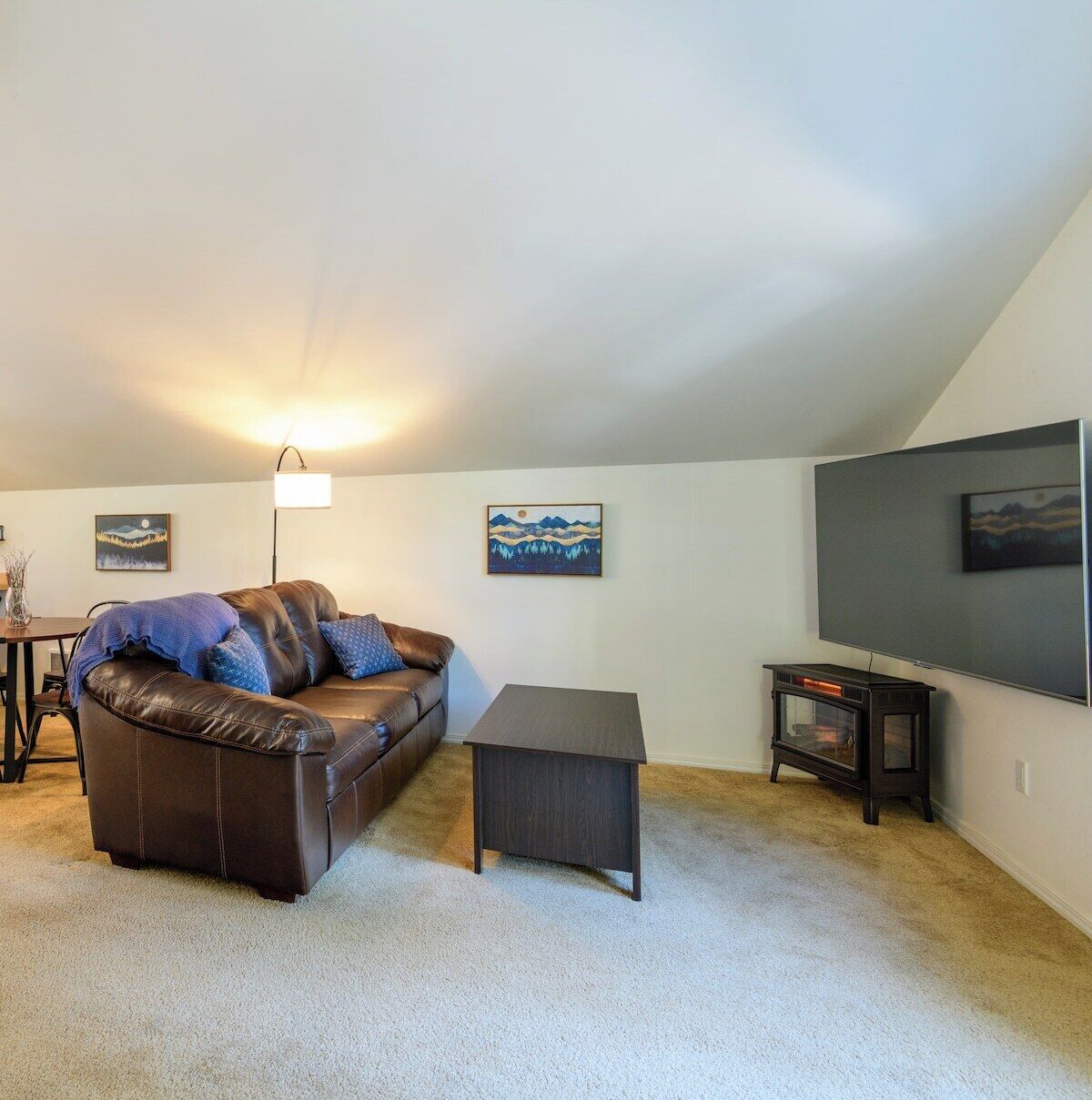 A living room with a brown leather couch, a small table, and a flat-screen TV mounted on the wall.