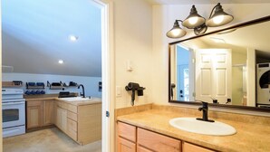 Una cocina con armarios de madera, un lavamanos blanco y un espejo grande con tres luces.