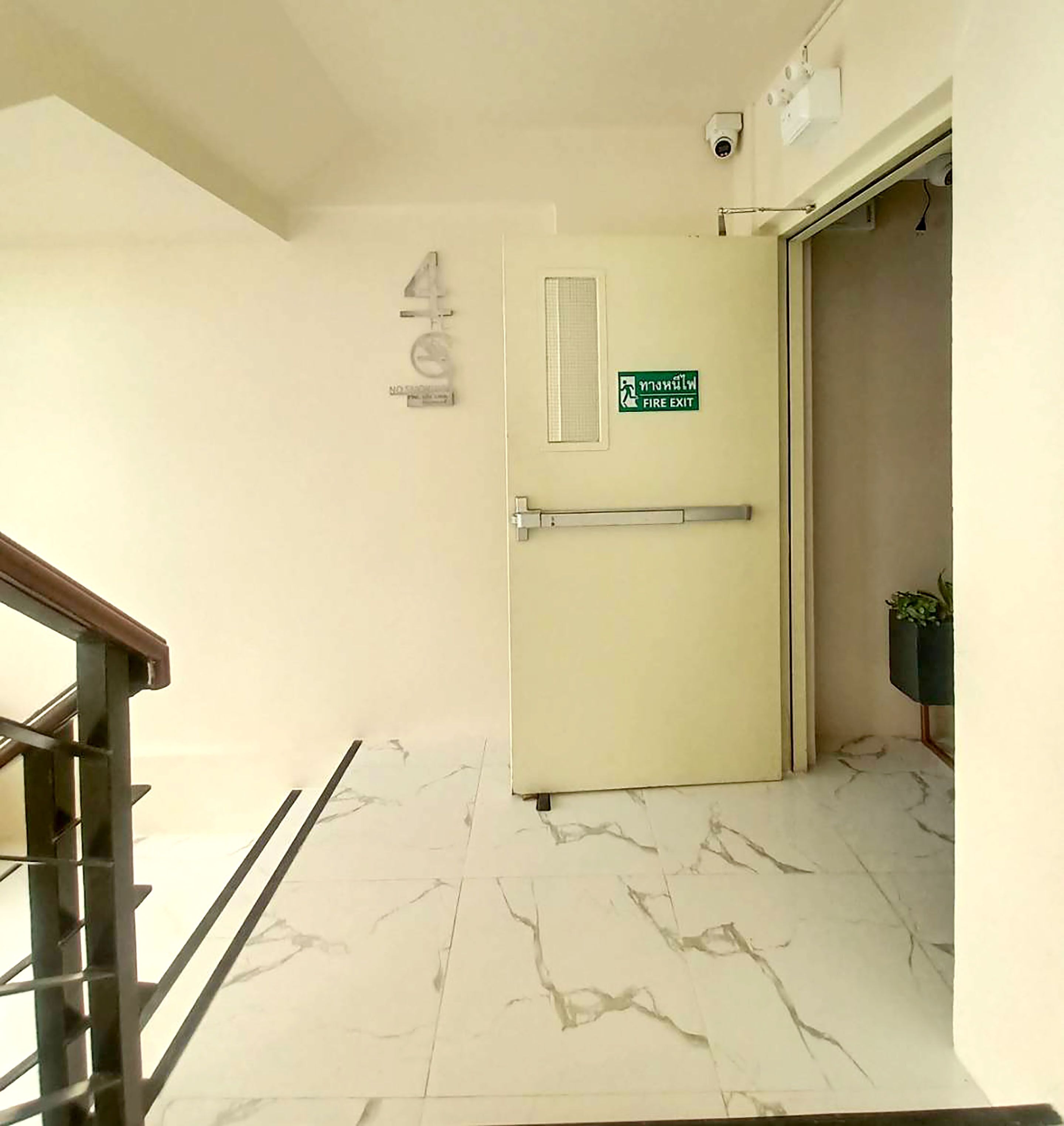 Un corridoio con pavimento in marmo, un cartello di uscita di sicurezza e una telecamera di sorveglianza.