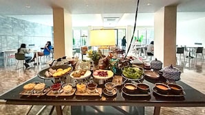 Mesa de buffet com diversos pratos e bebidas em um saguão moderno de hotel.