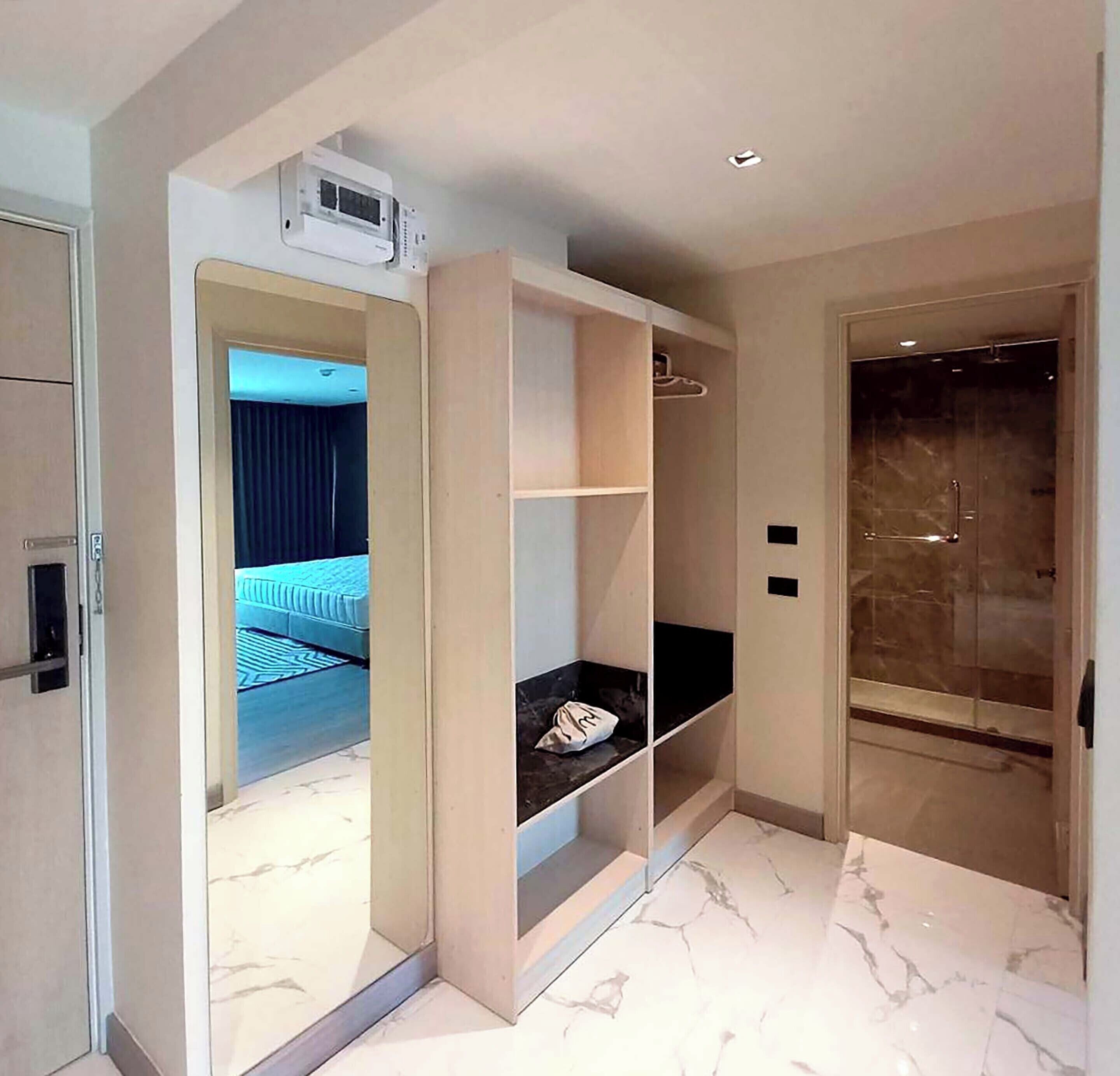 Una habitación de hotel moderna con piso de mármol, armario empotrado y baño separado con puerta de vidrio.