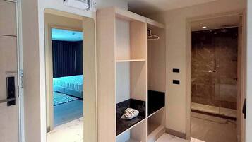 Une chambre d’hôtel moderne avec un sol en marbre, un placard intégré et une salle de bain séparée dotée d’une porte en verre.