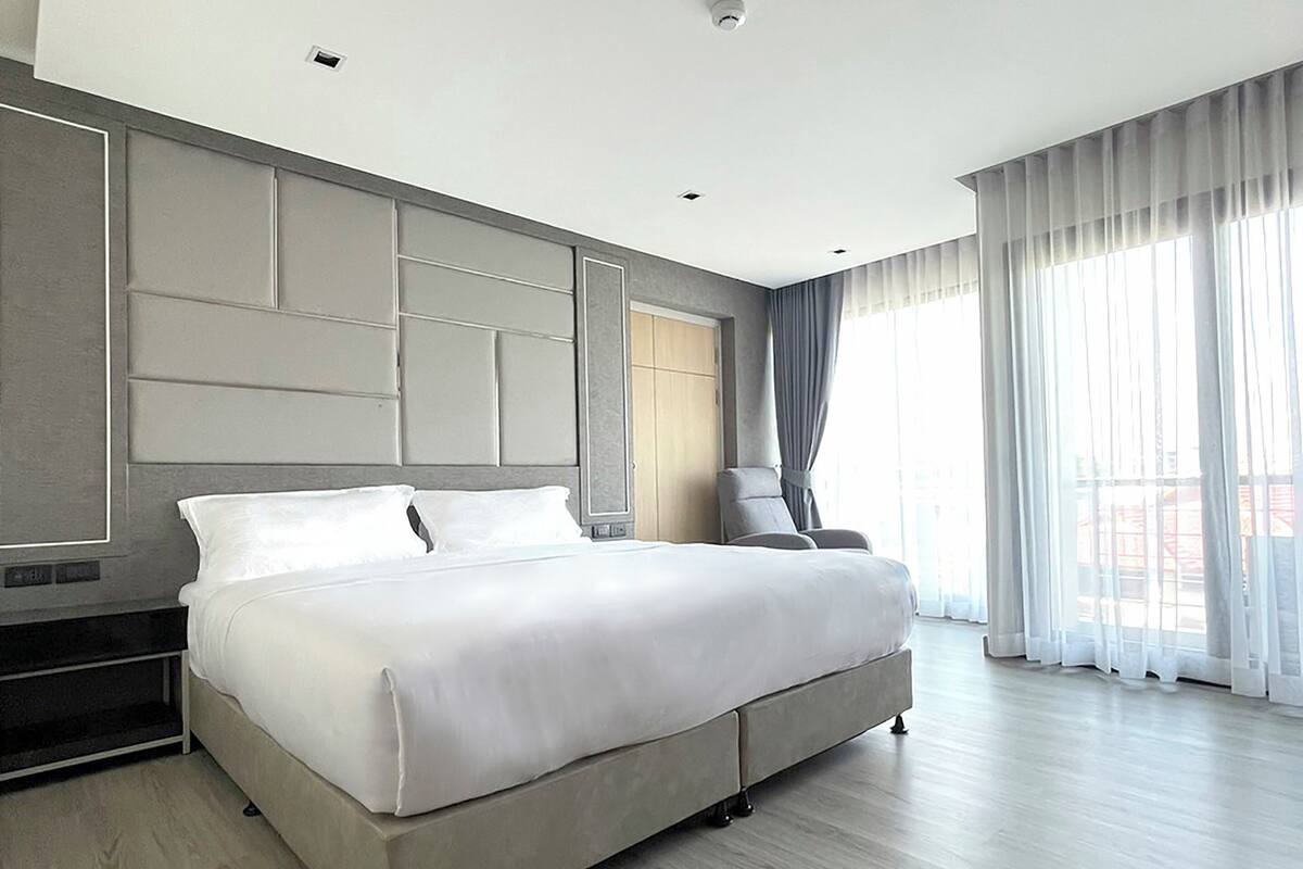 A modern hotel bedroom with a large bed, a seating area, and a view of the city.