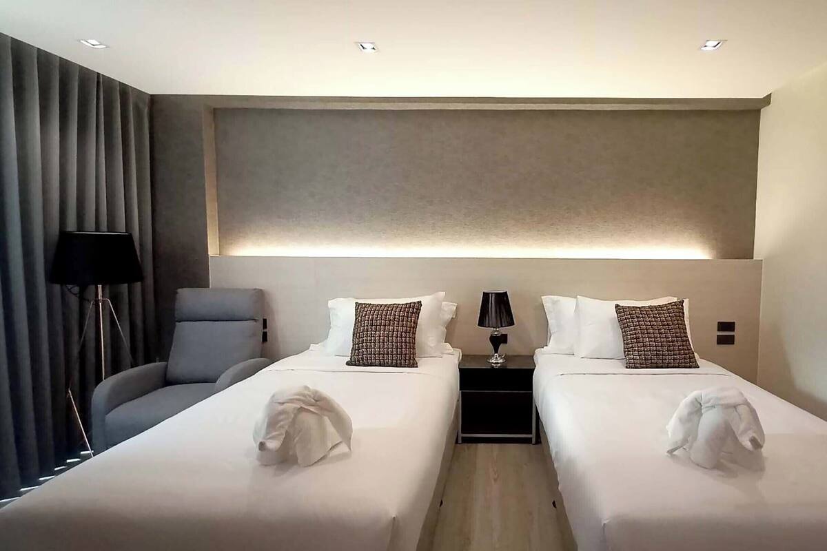 A modern hotel room with two beds, a desk, a chair, and a lamp.