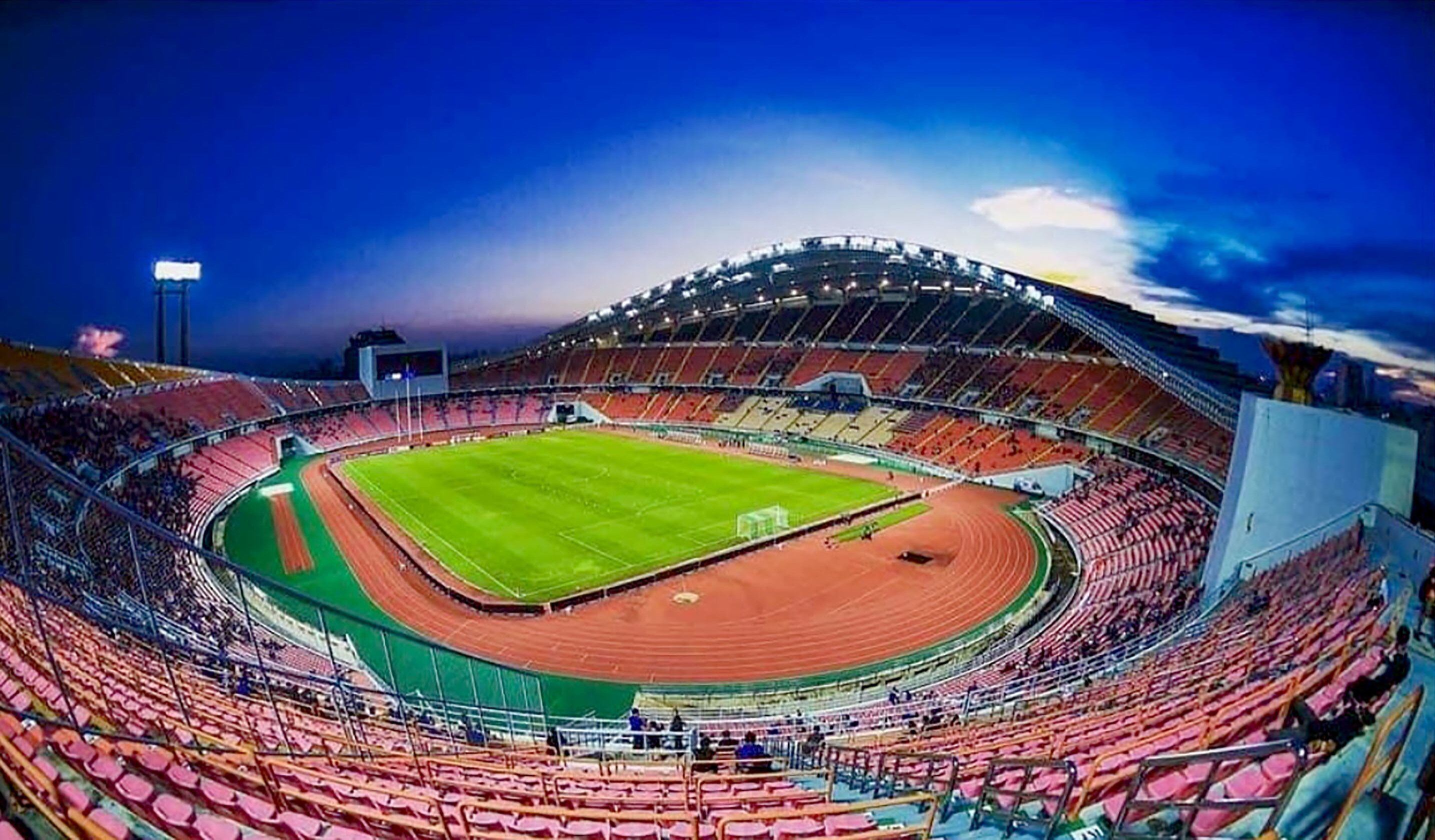 A large stadium with multiple tiers of seating, a central field, and a running track.