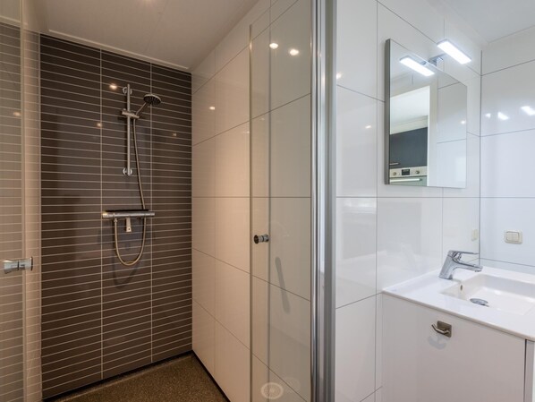 A modern bathroom with a glass-enclosed shower, a white sink, and a mirror above the sink.
