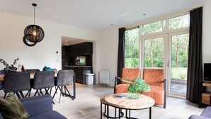 A modern living room with a sofa, a coffee table, and a dining area with chairs and a table. - Great chalet on park Drentheland (Zorgvlied)