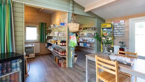 A cozy room with wooden walls and floors, a table with chairs, shelves with various items, and a refrigerator with beverages. - Great chalet on park Drentheland (Zorgvlied)