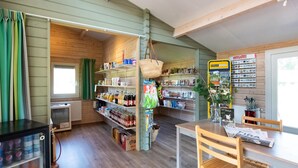 En mysig träinredd interiör med ett kylskåp, hyllor fyllda med snacks, ett bord med en stol och ett fönster med gardiner.
