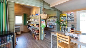 A cozy room with wooden walls and floors, a table with chairs, shelves stocked with various items, and a window with curtains. - Beautiful chalet with enclosed garden (Zorgvlied)