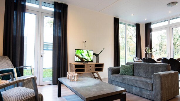 Una sala de estar moderna con sofá, sillón, mesa de centro y televisor sobre un soporte de madera.