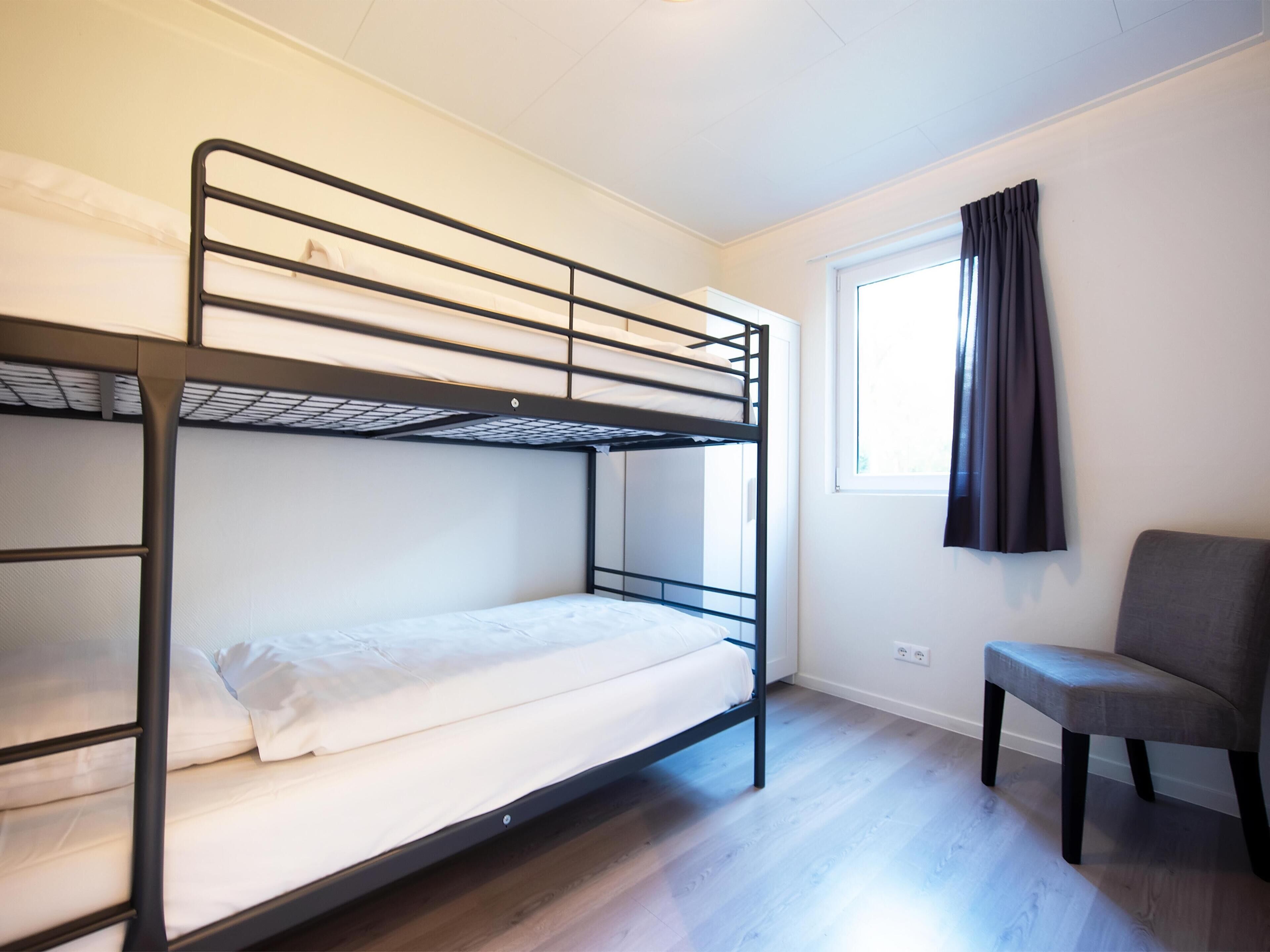 A bunk bed room with a window and a chair.