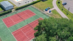 Vista aérea de un complejo deportivo con cancha de tenis, piscina y edificios circundantes.