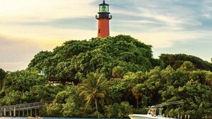 Un faro en una pequeña isla rodeada de abundante vegetación y un mar tranquilo.