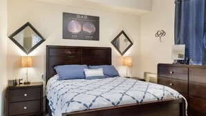Un dormitorio con cama, dos mesitas de noche, cómoda y decoración en la pared.