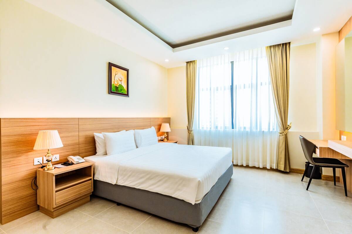 Une chambre d’hôtel avec un grand lit, des tables de chevet avec des lampes, un bureau et une chaise.