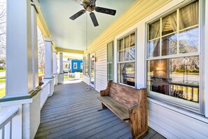 A covered porch with a wooden bench, large windows, and a ceiling fan.