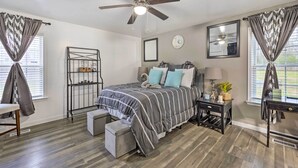 A bedroom with a bed, a nightstand, a chair, a small table, a ceiling fan, a window with curtains, a wall clock, and a shelf with items. - Richmond Home with Pool, 5 Mi to Downtown! (Richmond)