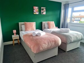 Ein Hotelzimmer mit zwei Betten, grünen Wänden und einem Fenster mit Vorhängen.