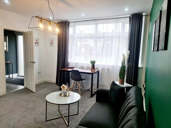 Ein modernes Wohnzimmer mit einer Couch, einem runden Couchtisch, einem Esstisch mit Stühlen und einem großen Fenster mit Vorhängen.