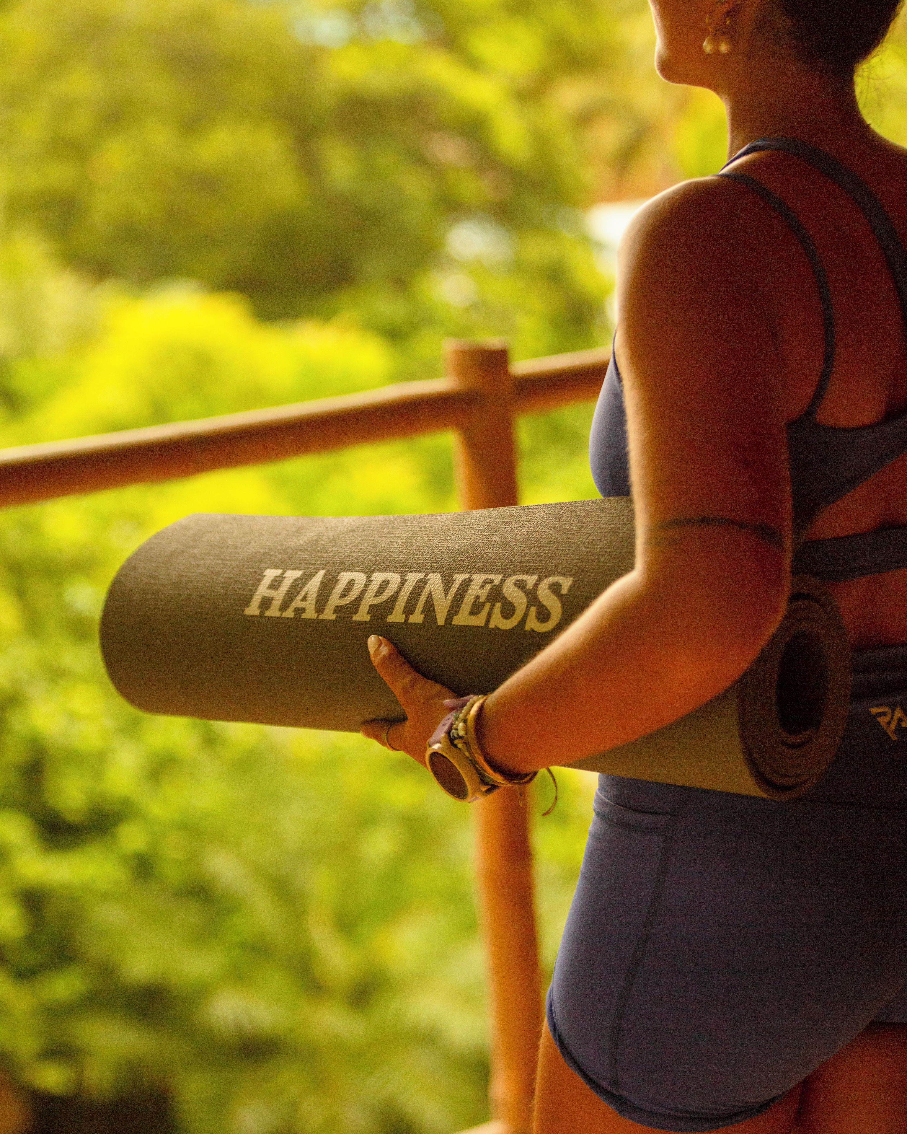 A person holding a yoga mat with the word 'HAPPINESS' on it.