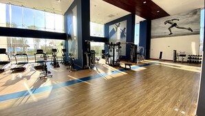 A spacious gym with cardio machines, weightlifting equipment, and a large mural on the wall. - Camino al Mar, Apartment on the Beach with Fabulous Amenities Zona Dorada Pure Luxury (Mazatlán)