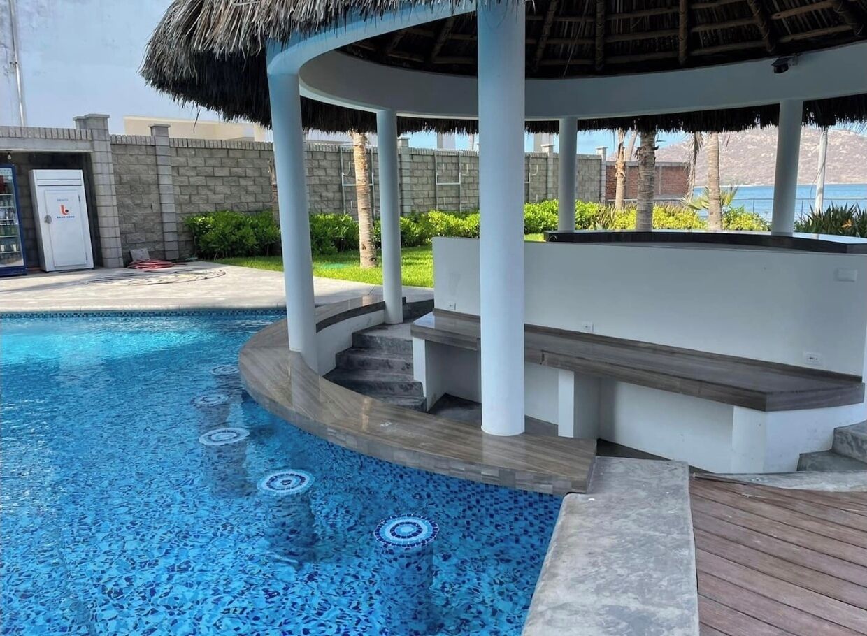 A swimming pool with a thatched roof seating area, a water fountain, and a view of the sea.
