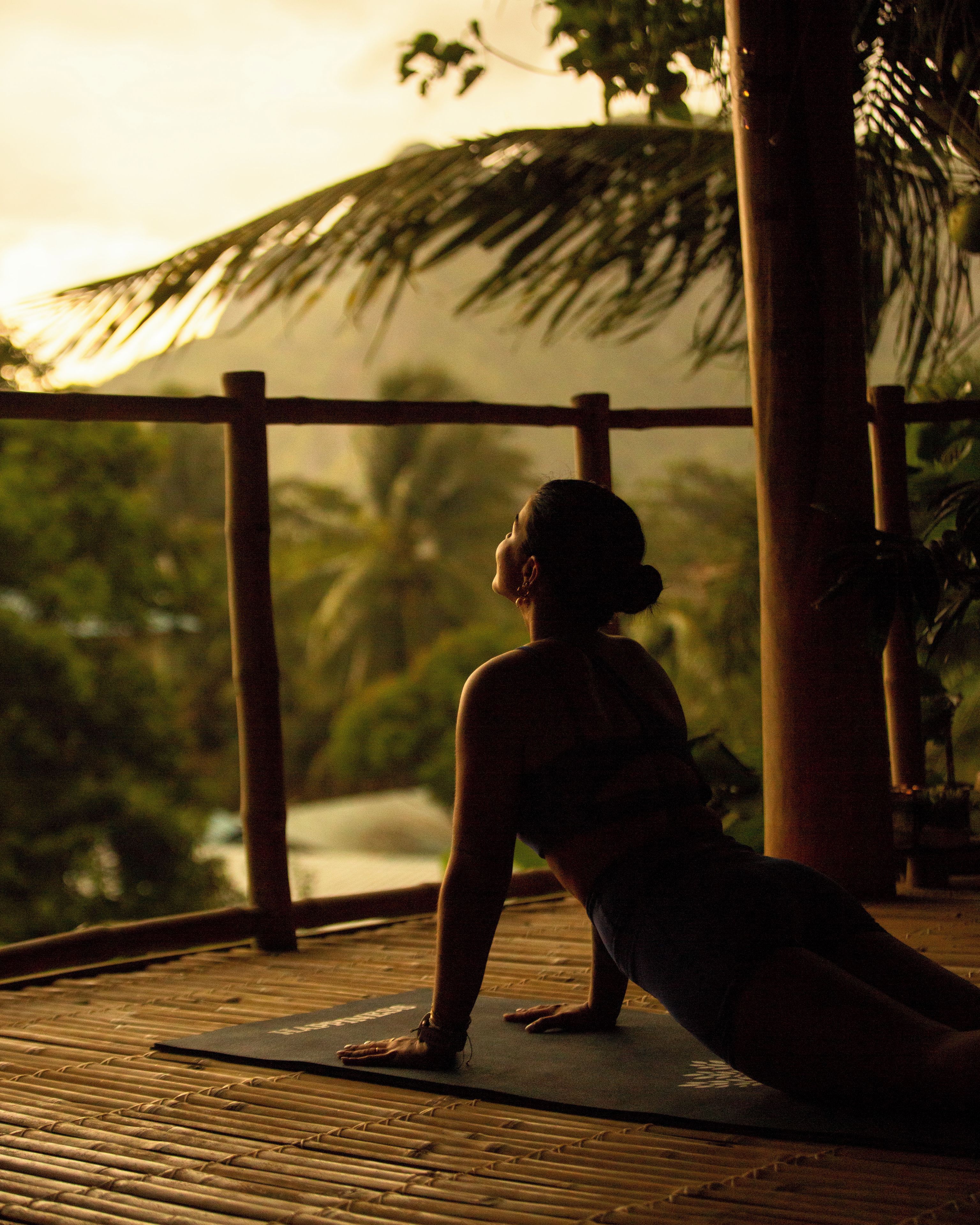 Una persona realizando una postura de yoga sobre una esterilla al aire libre.
