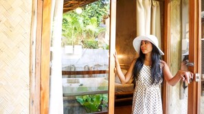 A woman in a polka dot dress and white hat standing at a wooden door, holding a key. - Happiness Native Villa (El Nido)