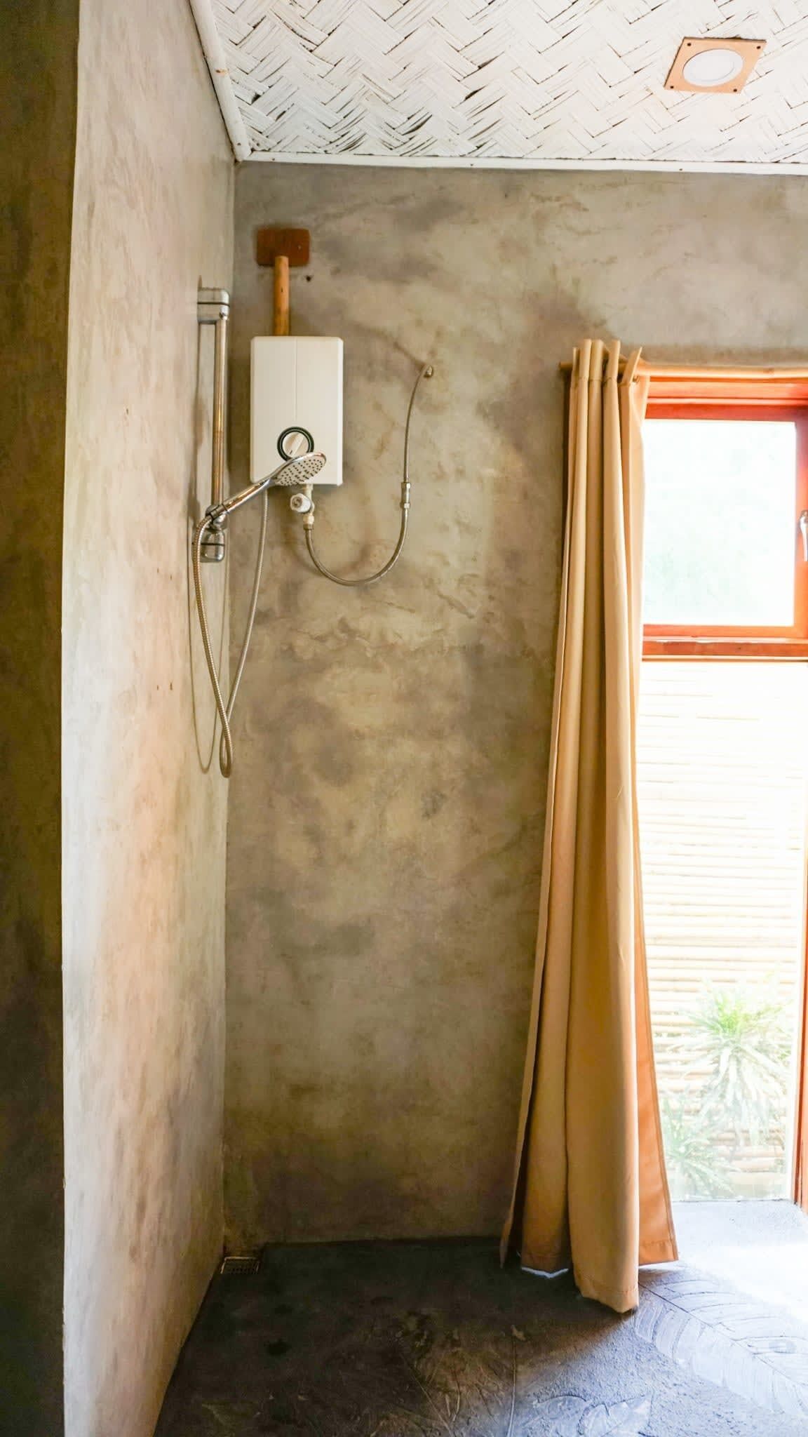 Une salle de bain avec une douche, une fenêtre avec des rideaux et un chauffe-eau visible.