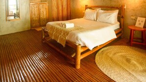 A room with a bed, wooden floor, and a thatched ceiling.