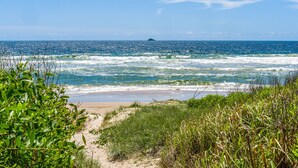 Une plage avec un sentier sablonneux menant à l’océan, entourée de verdure.