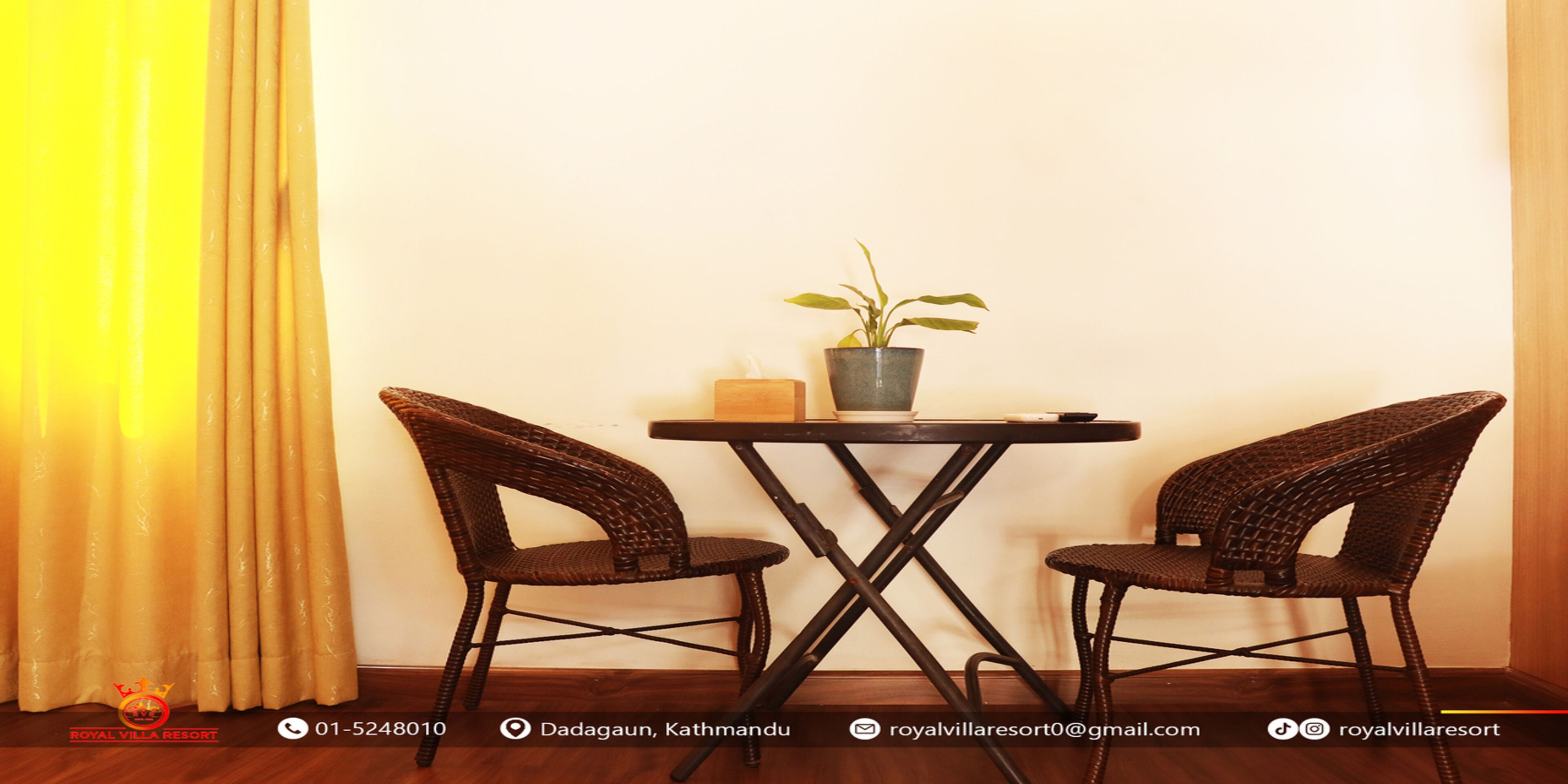 A room with a small table and two wicker chairs, a potted plant, and a curtain.
