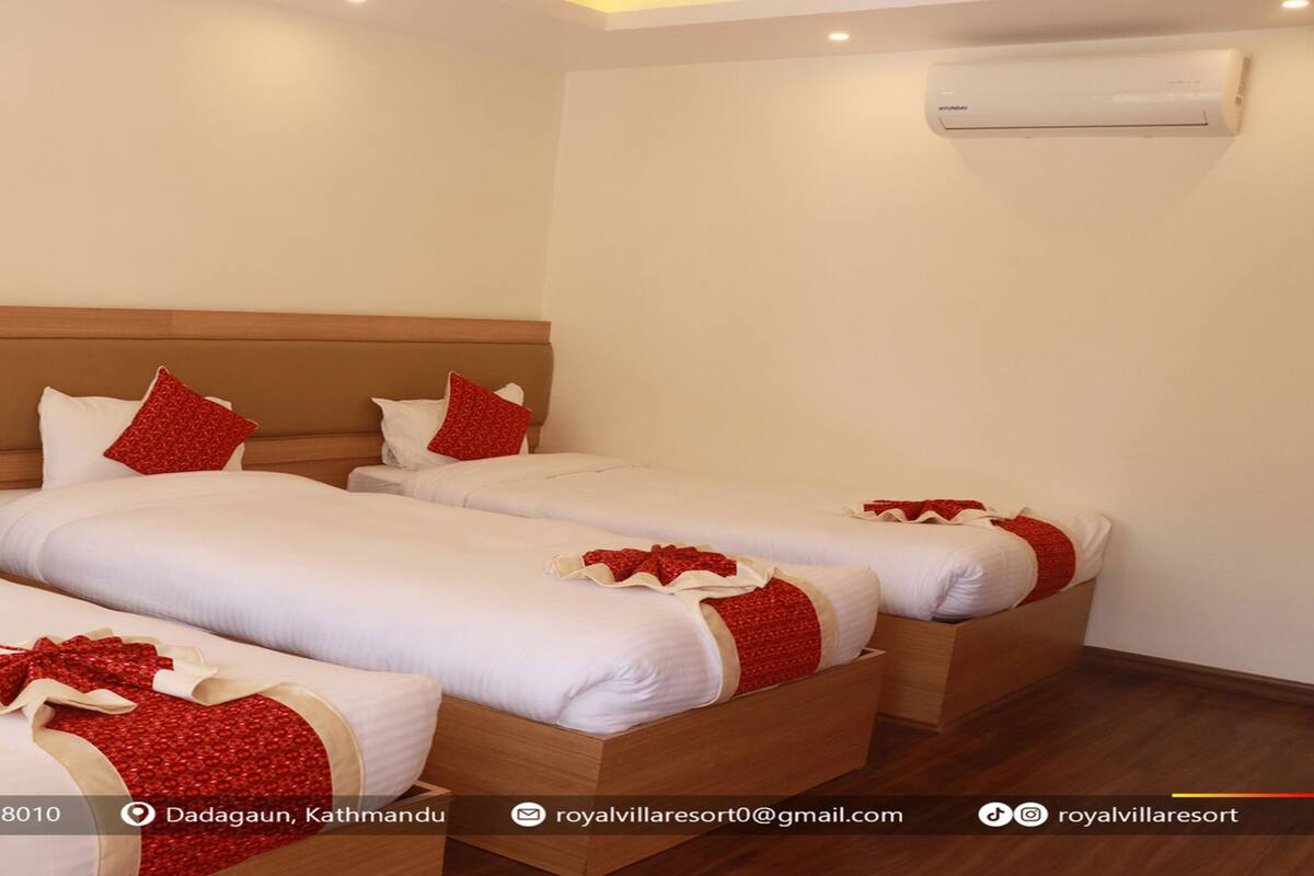 A hotel room with three single beds, each with white bedding and red accents. There is a wooden headboard, an air conditioning unit on the wall, and a logo on the wall.