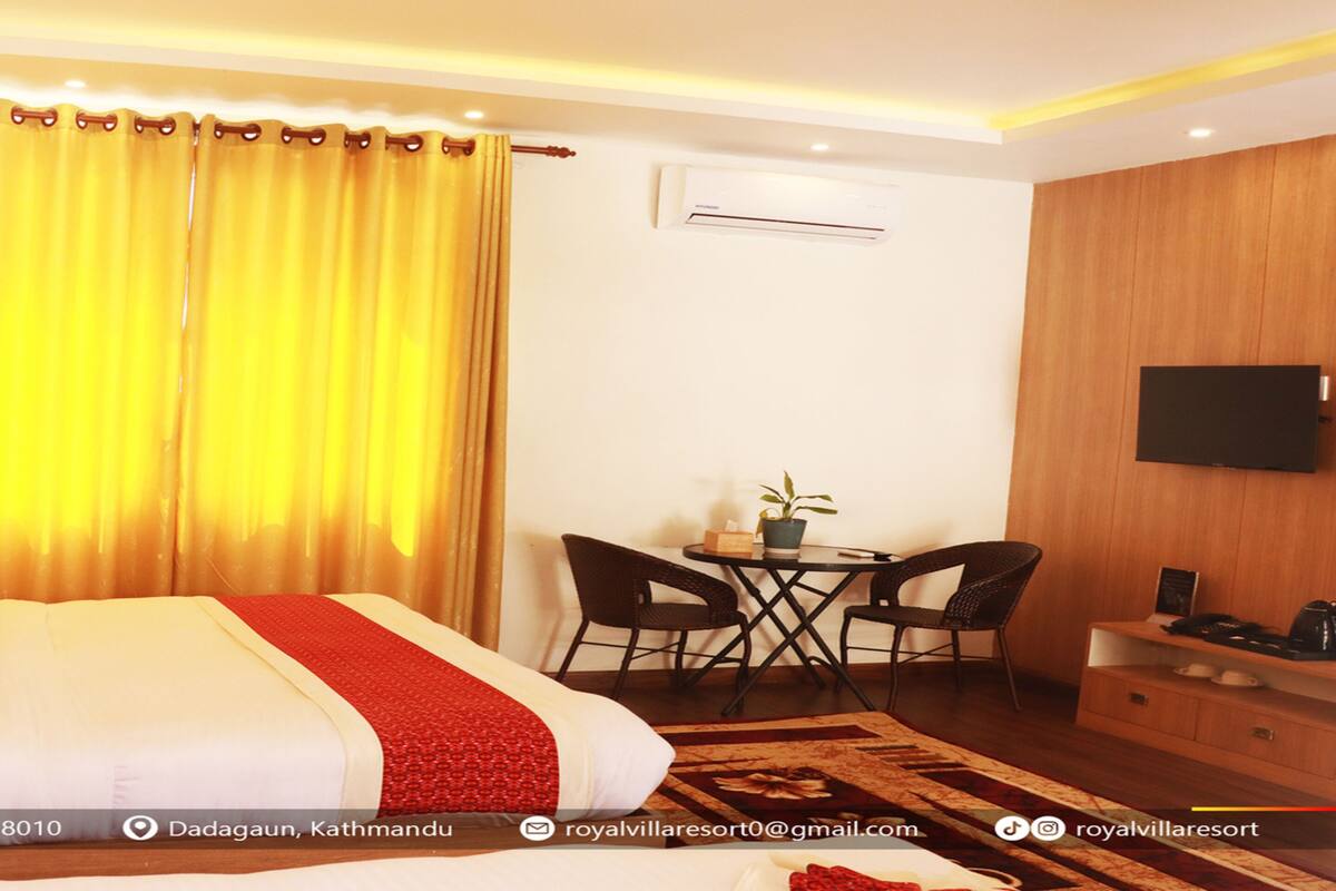 A hotel room with a large bed, a desk with two chairs, a television, and an air conditioning unit.