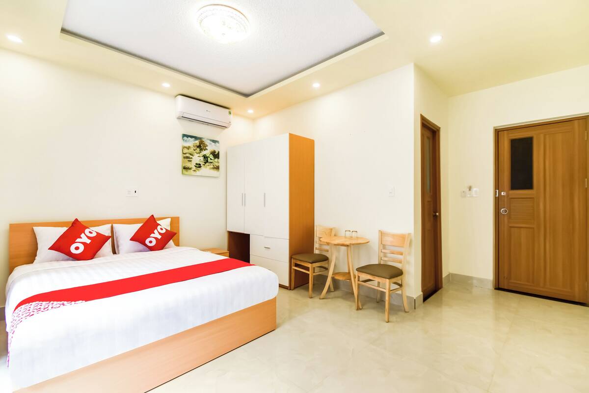 A hotel room with a bed, a desk, two chairs, a wardrobe, and a door.