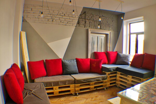 Un salon moderne avec un canapé d’angle, des coussins rouges et gris, et un plancher en bois.
