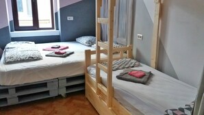 A room with two bunk beds, each with a mattress and pillows, and a window providing natural light.