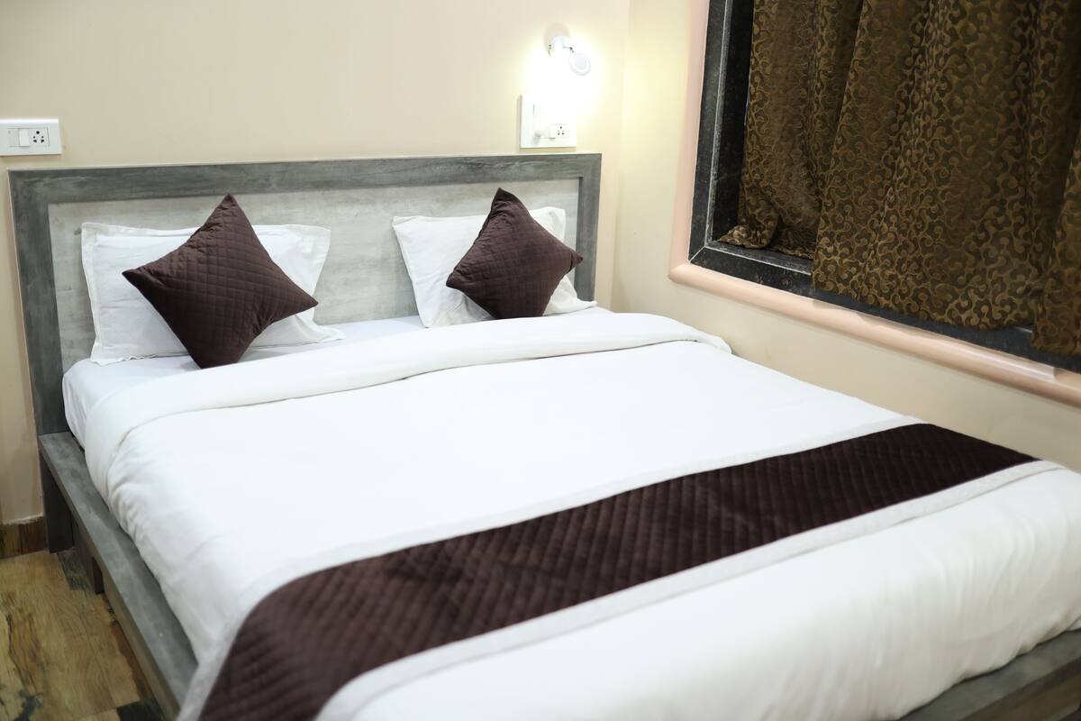 Uma cama bem arrumada com roupa de cama branca e marrom, uma cabeceira de madeira e uma janela com cortinas.