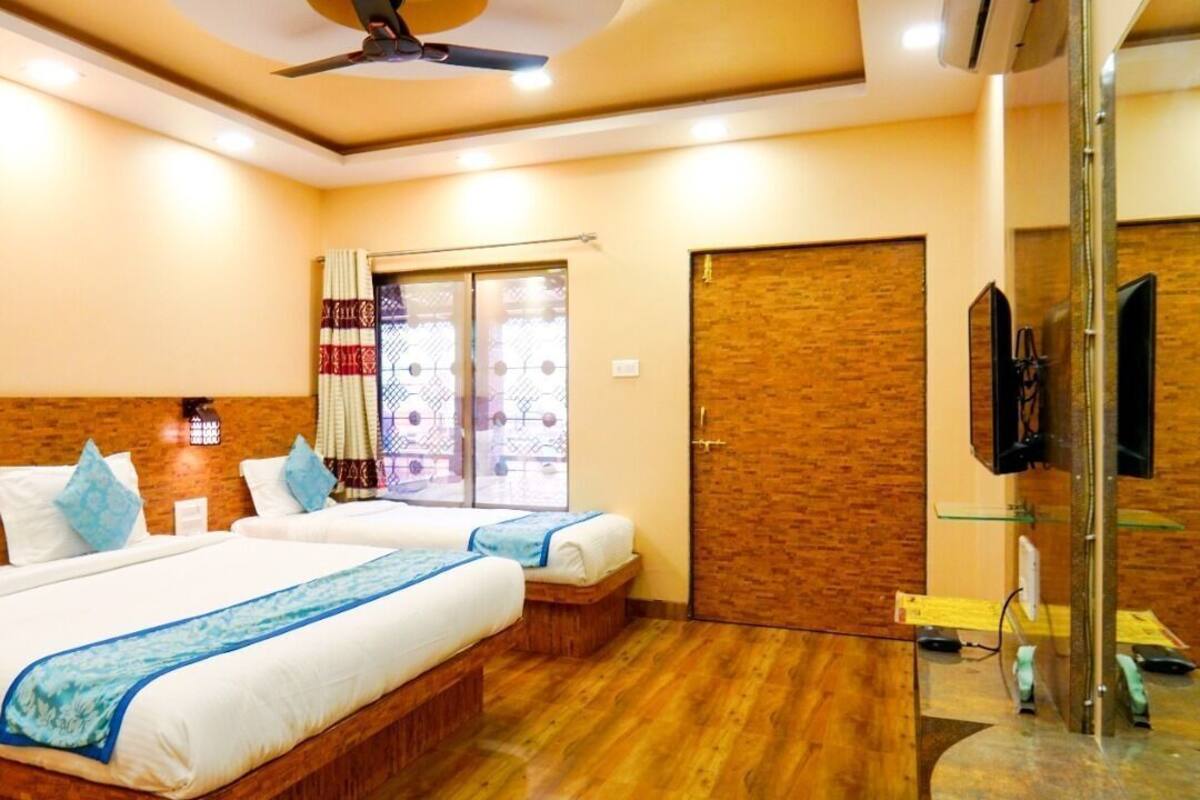 Quarto de hotel com duas camas, televisão, ventoinha no teto e janela com cortinas.