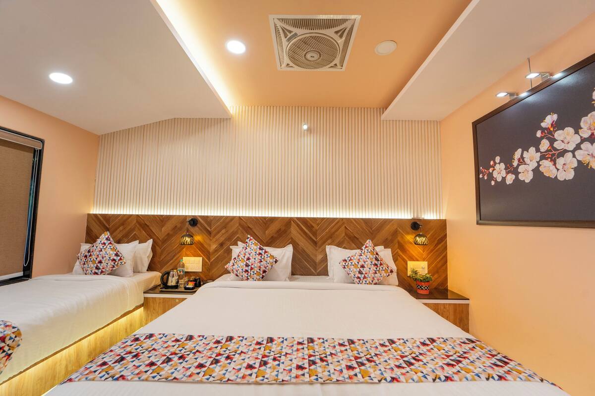 Quarto de hotel com duas camas, uma cabeceira de madeira, um painel decorativo na parede, um ventilador de teto e uma TV fixada na parede.