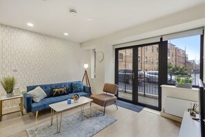 Relax in this stylish living room with a blue sofa, coffee table, and armchair, featuring a patterned wall and a large window with a view of the street.